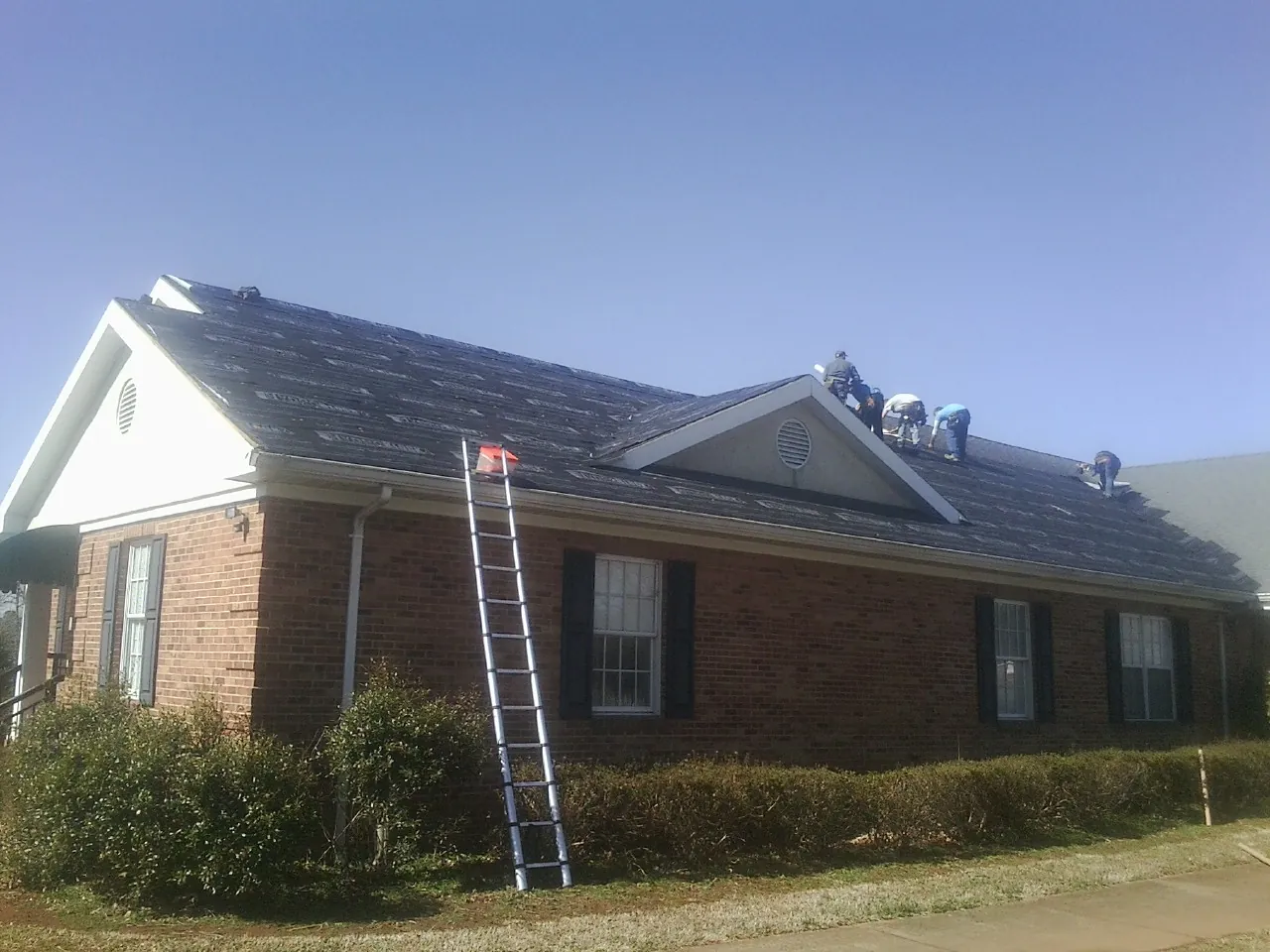 Crew tearing shingles off a brick ranch roof with a ladder set — Emergency Roof Repair work by our crew in New Castle