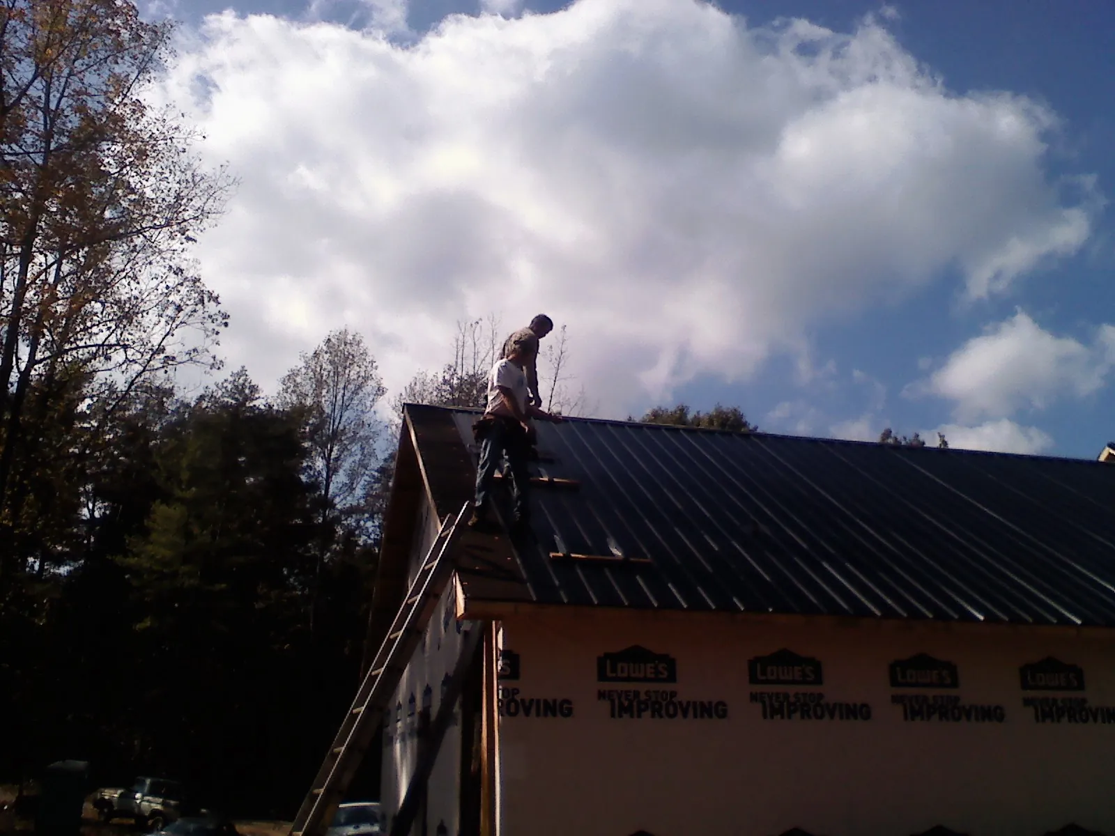 Roofer fastening dark metal panels high against a cloudy sky, from a Roof Inspection job in New Castle